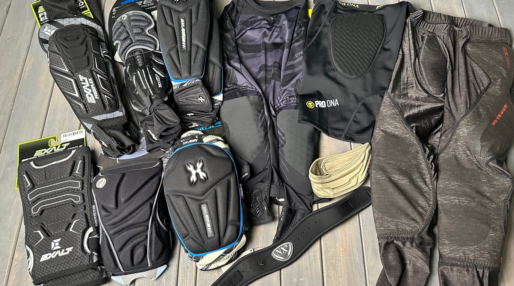 A photo of different paintball protective gear. Arm pads, knee pads, slide shorts, slide pants all adorn the table.