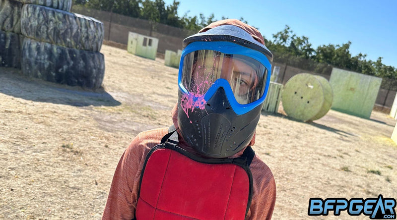 A paintball player wearing an approved paintball safety goggle that has a bright pink hit on the goggle.