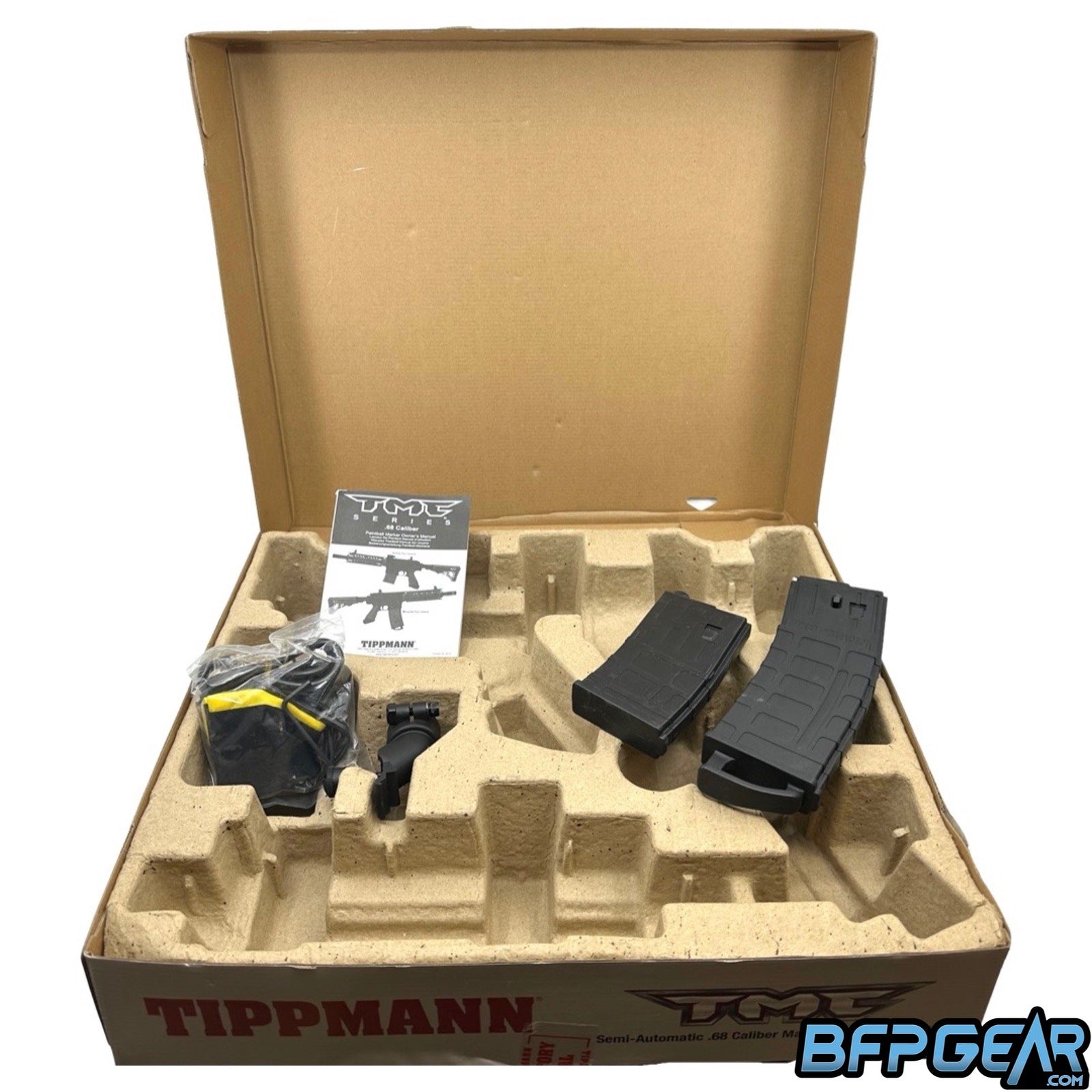 The packaging of the Tippmann TMC. Cardboard mold holds the marker and accessories easily. Included is an extra magazine, hopper adaptor, barrel sock, barrel squeegee, spare parts, Allen keys, and a user manual. The magazines for the Dark Earth TMC will be tan instead of black.