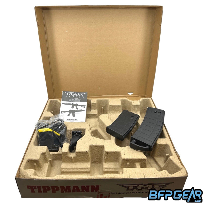 The packaging of the Tippmann TMC. Cardboard mold holds the marker and accessories easily. Included is an extra magazine, hopper adaptor, barrel sock, barrel squeegee, spare parts, Allen keys, and a user manual. The magazines for the Dark Earth TMC will be tan instead of black.