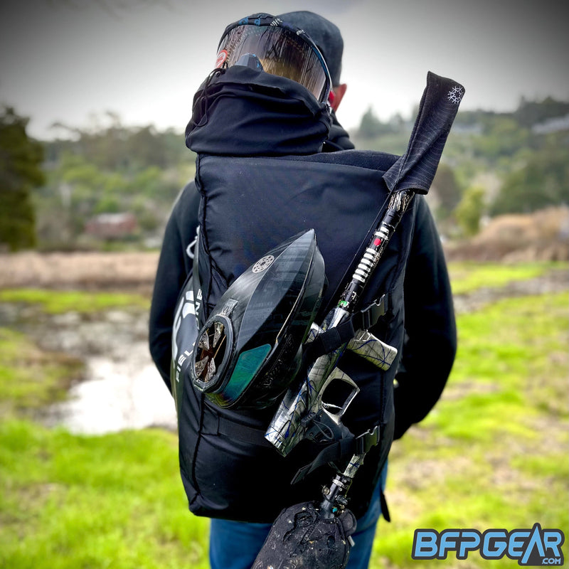 A photo of the AW backpack on a person. The person is facing away, showing the backpack off with a goggle system and full marker setup secured to the backpack.